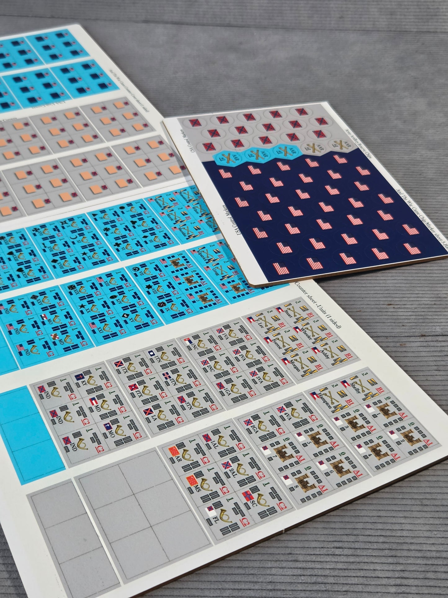 Three sheets of decorative adhesive stickers or decals laid out on a gray wood-textured surface. The sheets feature various geometric patterns, including blue, pink, red, and gray designs.