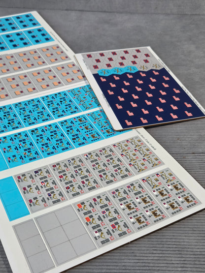 Three sheets of decorative adhesive stickers or decals laid out on a gray wood-textured surface. The sheets feature various geometric patterns, including blue, pink, red, and gray designs.