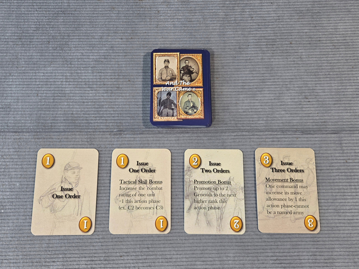 A set of four illustrated cards laid out on a gray textured surface, with a small blue card stack or box centered above them. The cards show vintage-style portraits and text, including titles such as Issue One Order and Issue Two Orders.