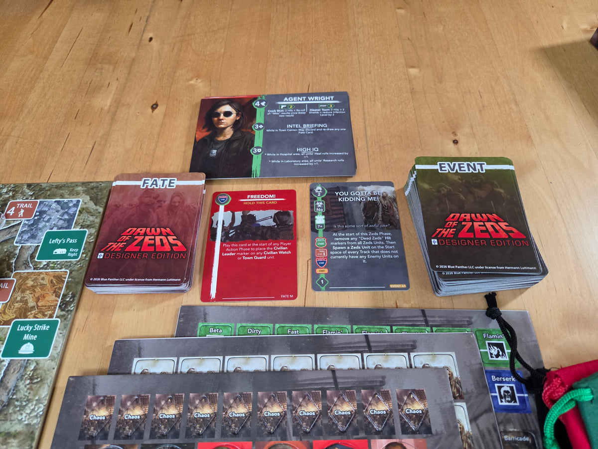 A tabletop spread of the board game "Dawn of the Zeds," showing various cards, action tiles, and stacks of game components arranged on a light wood floor.