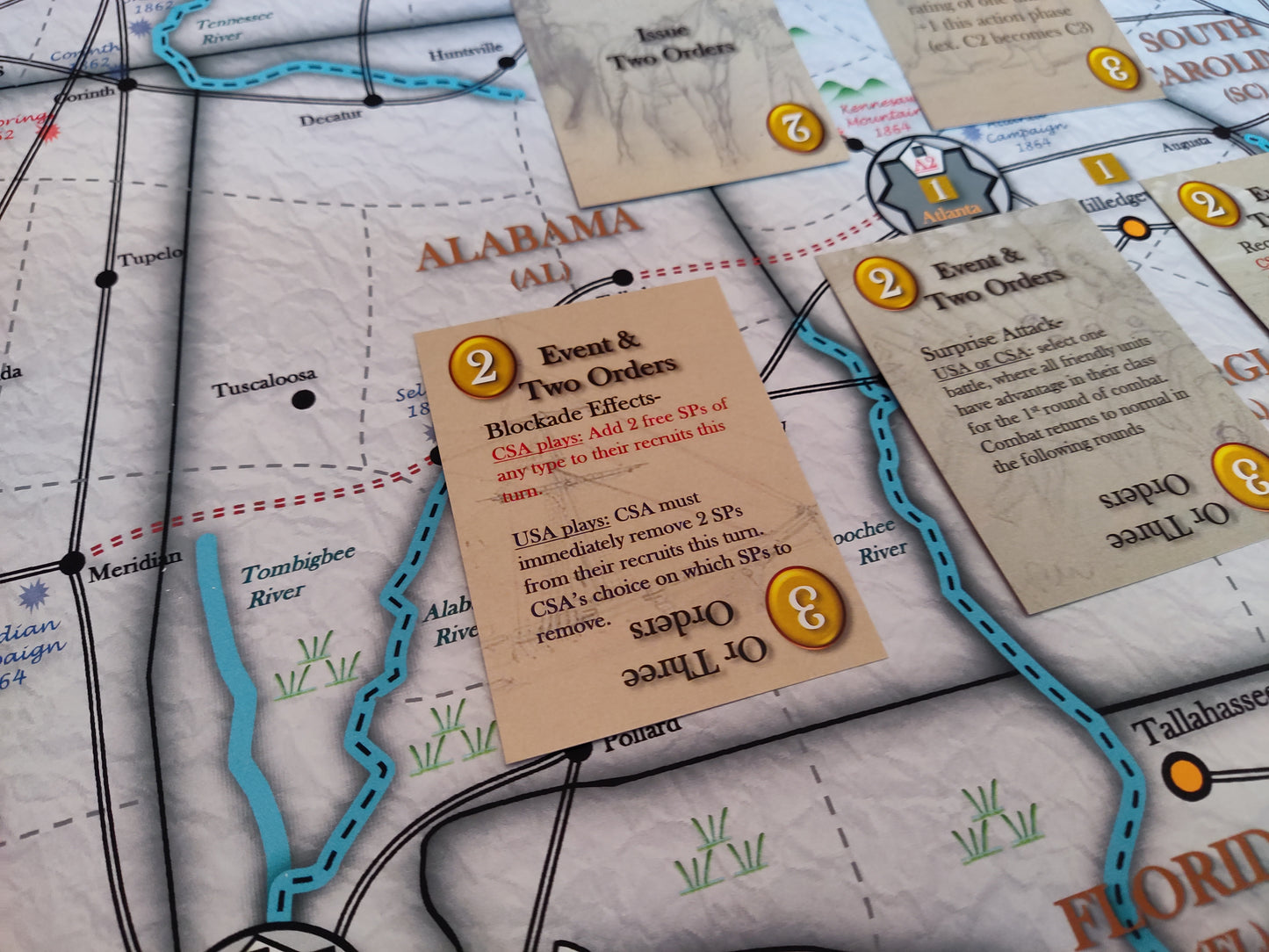 Board game components on a map of Alabama with cards and markers.